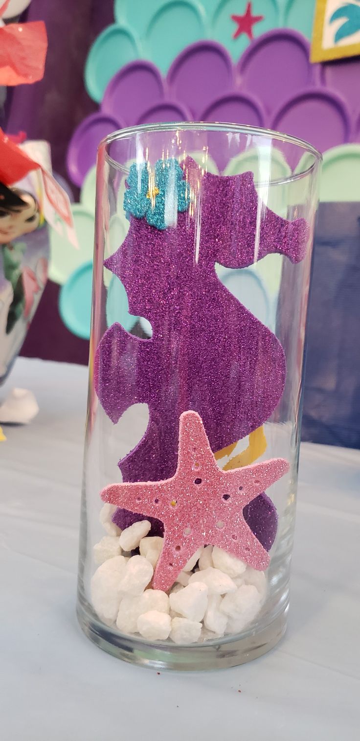 a glass filled with white rocks and purple glittered seahorse on top of it