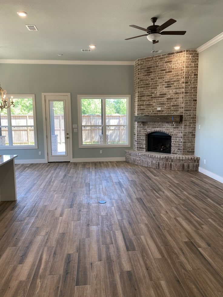 an empty living room with wood flooring and a brick fireplace in the center area