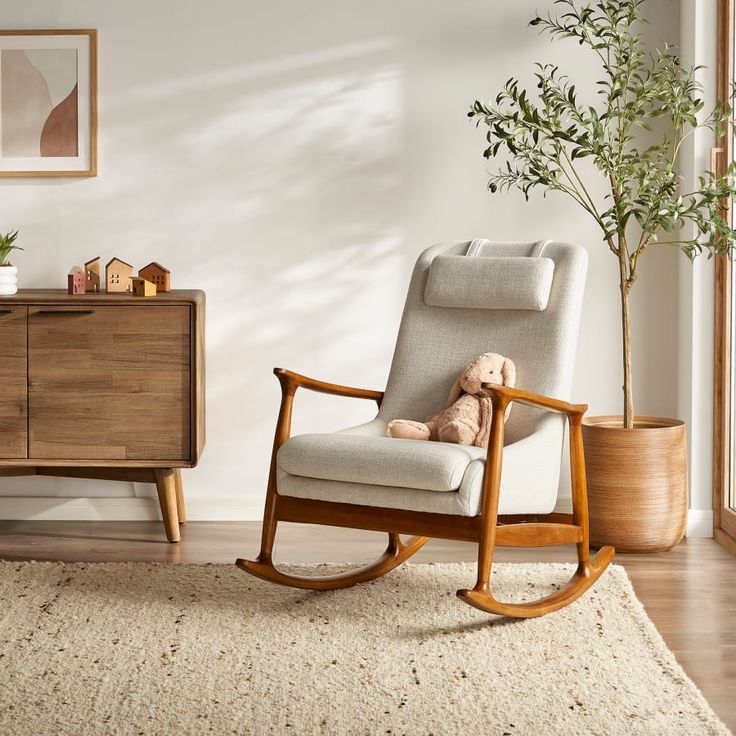 a rocking chair with a teddy bear on it next to a dresser and potted plant