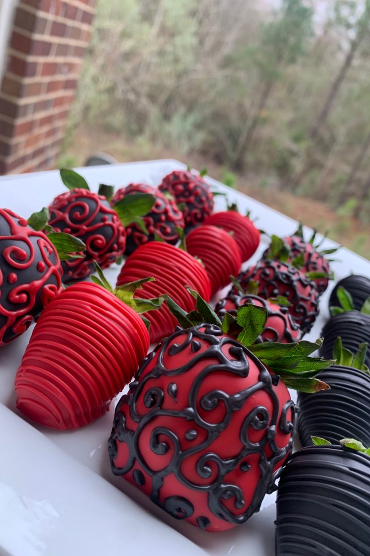 chocolate covered strawberries are arranged on a white platter with black and red decorations