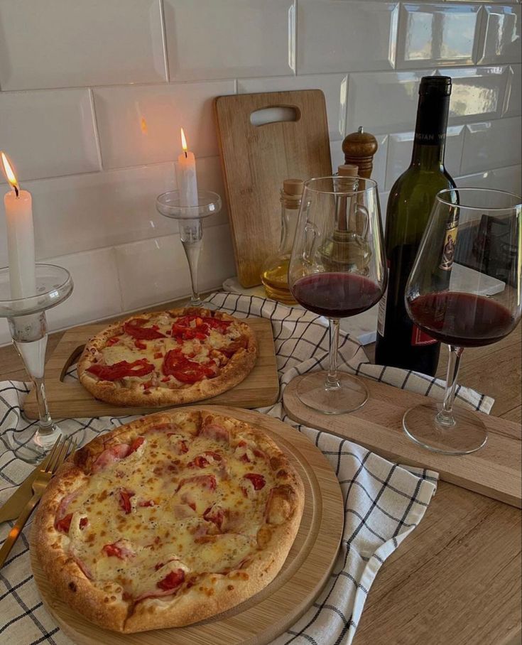 two pizzas sitting on top of wooden cutting boards next to wine glasses and candles