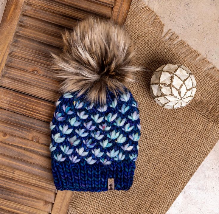 a knitted hat with a pom - pom sits on top of a rug