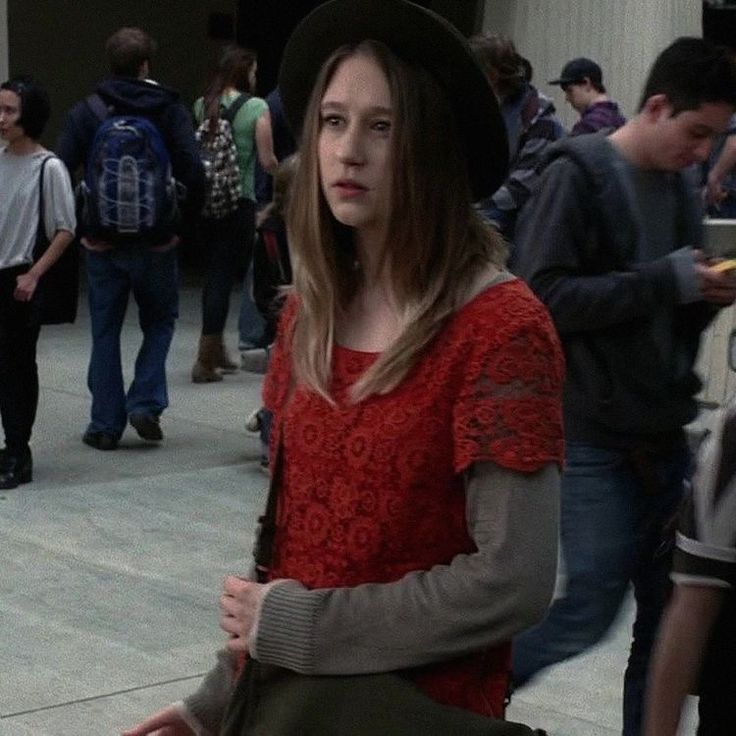 a woman in a red sweater and black hat is standing on the sidewalk with other people