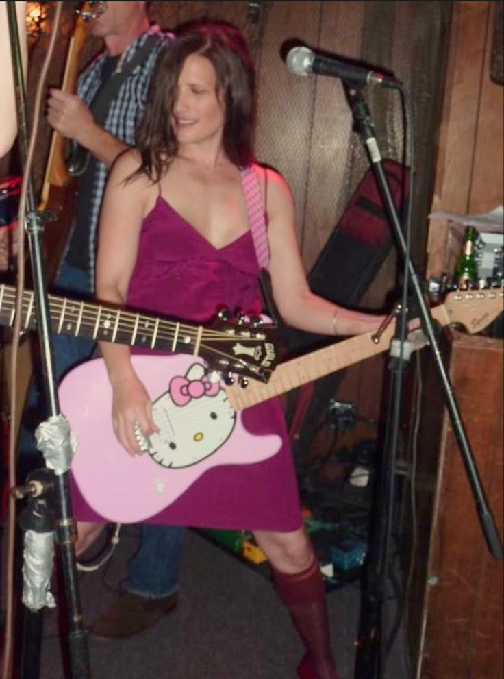 a woman in a pink dress holding a hello kitty guitar and singing into a microphone