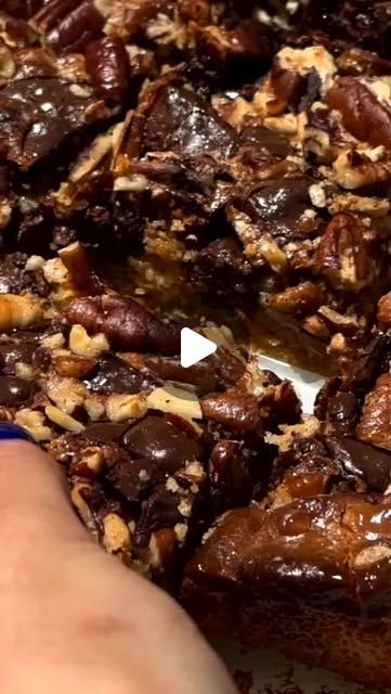 someone cutting into a chocolate dessert with pecans on the top and bottom pieces missing