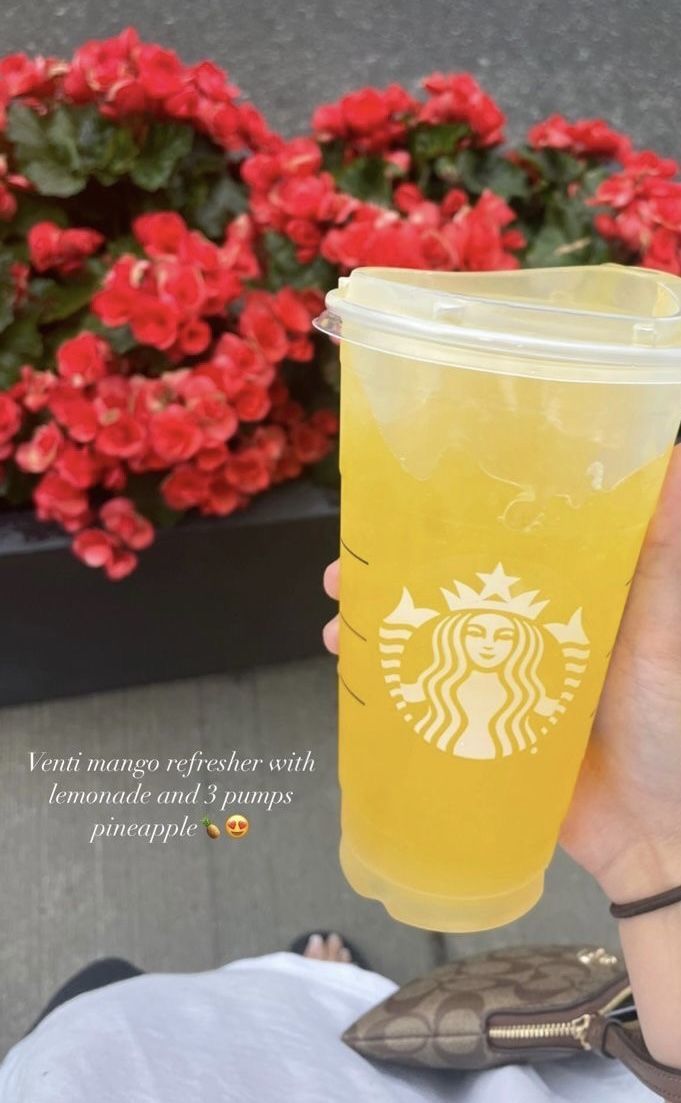 a person holding up a starbucks drink in front of some flowers