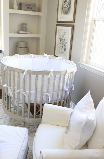 a baby crib in the corner of a living room with white furniture and pillows