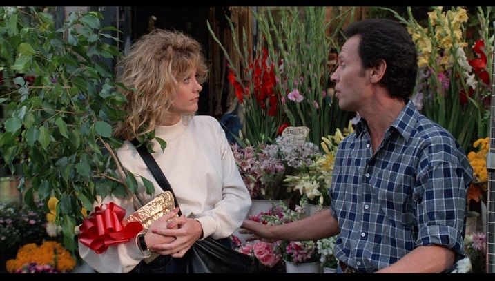 a man standing next to a woman holding a red bow in her hand and flowers behind her