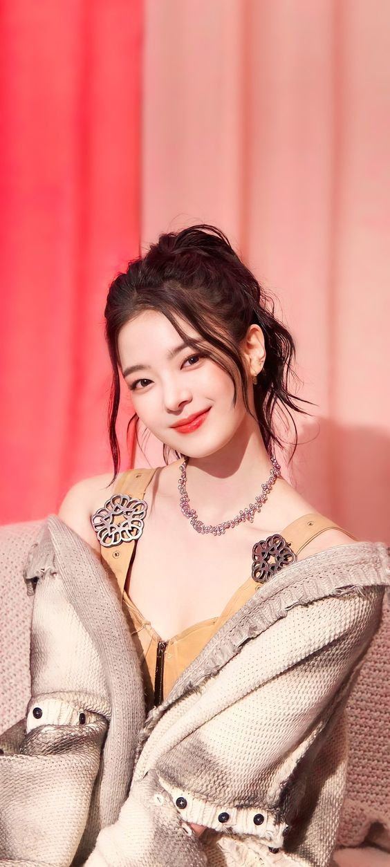 a woman sitting on top of a couch next to a red curtain and wearing a necklace