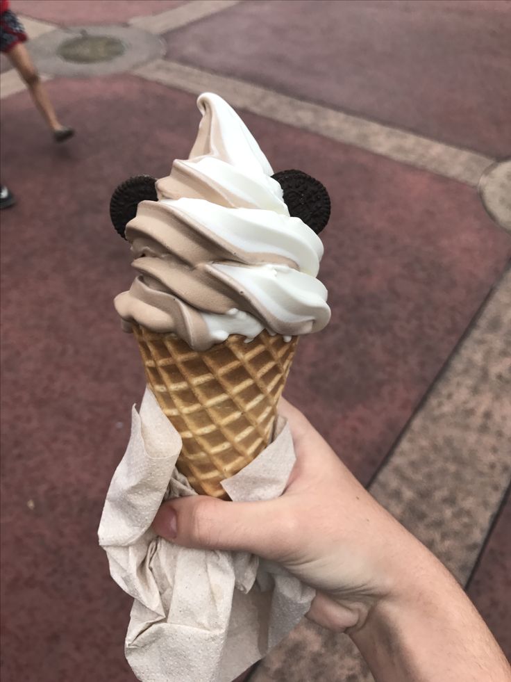 a hand holding an ice cream cone with mickey mouse on top