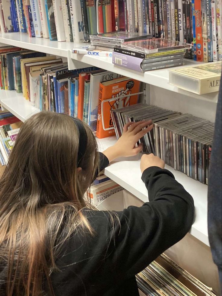 a woman is looking at cd's on a shelf in a library with other books