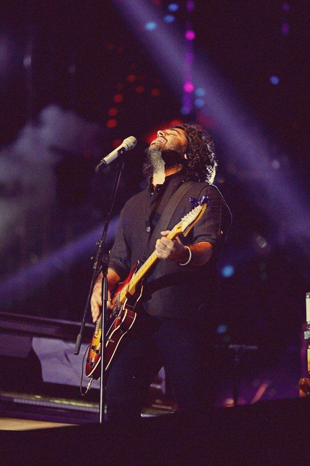 a man with long hair and beard holding a guitar in front of a microphone on stage