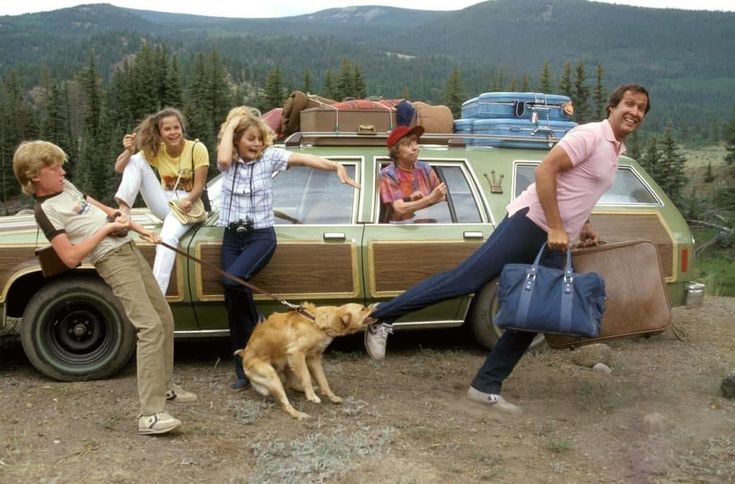 a group of people standing next to a car with luggage on it and a dog