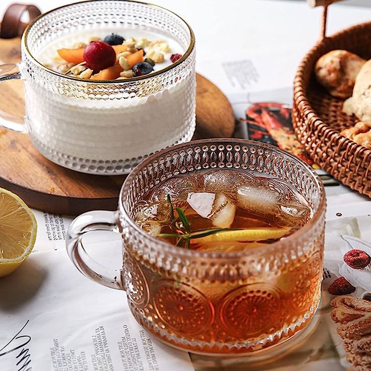 two glasses of tea sit on a table with bread and pastries in the background