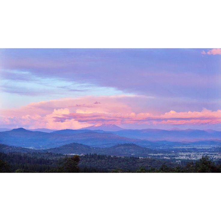 the sky is pink and blue as the sun sets over some mountains in the distance