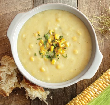 a white bowl filled with corn on the cob next to a piece of bread