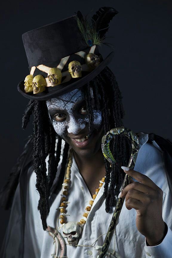 a man with dreadlocks and painted face holding a snake in his right hand