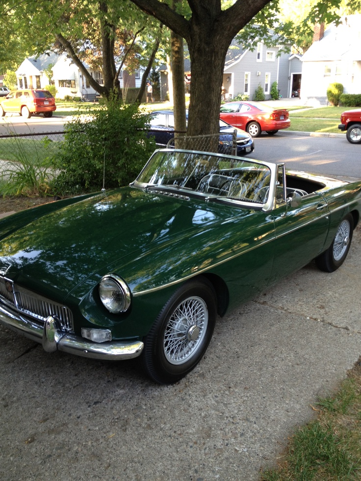 an old green car is parked on the side of the road next to a tree