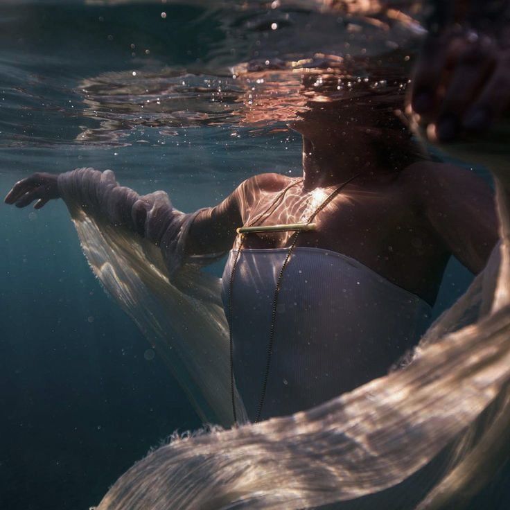 a woman in white swimsuit floating under water with her arms wrapped around the waist