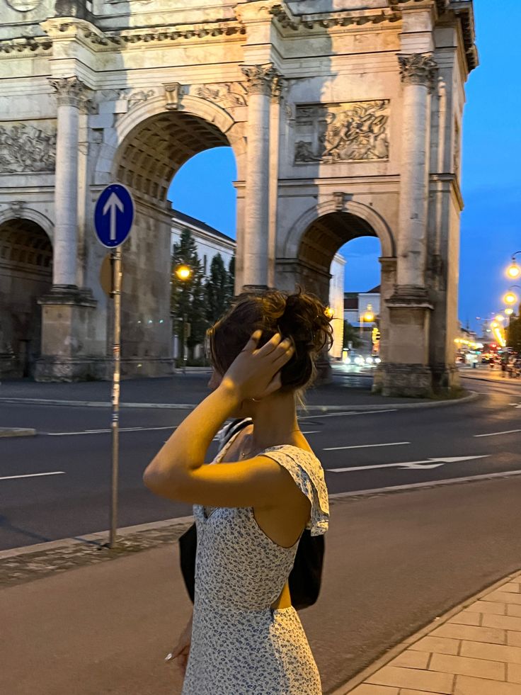 a woman standing on the side of a road talking on a cell phone next to an arch