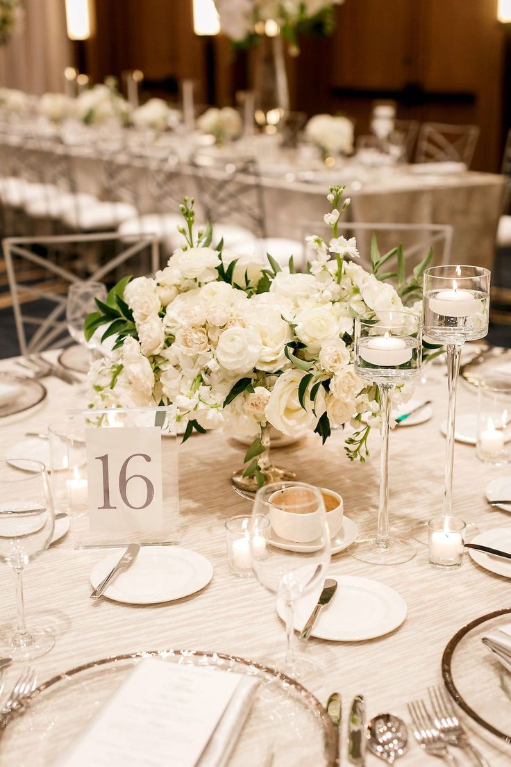 the table is set with silverware and white flowers in vases, candles and place cards