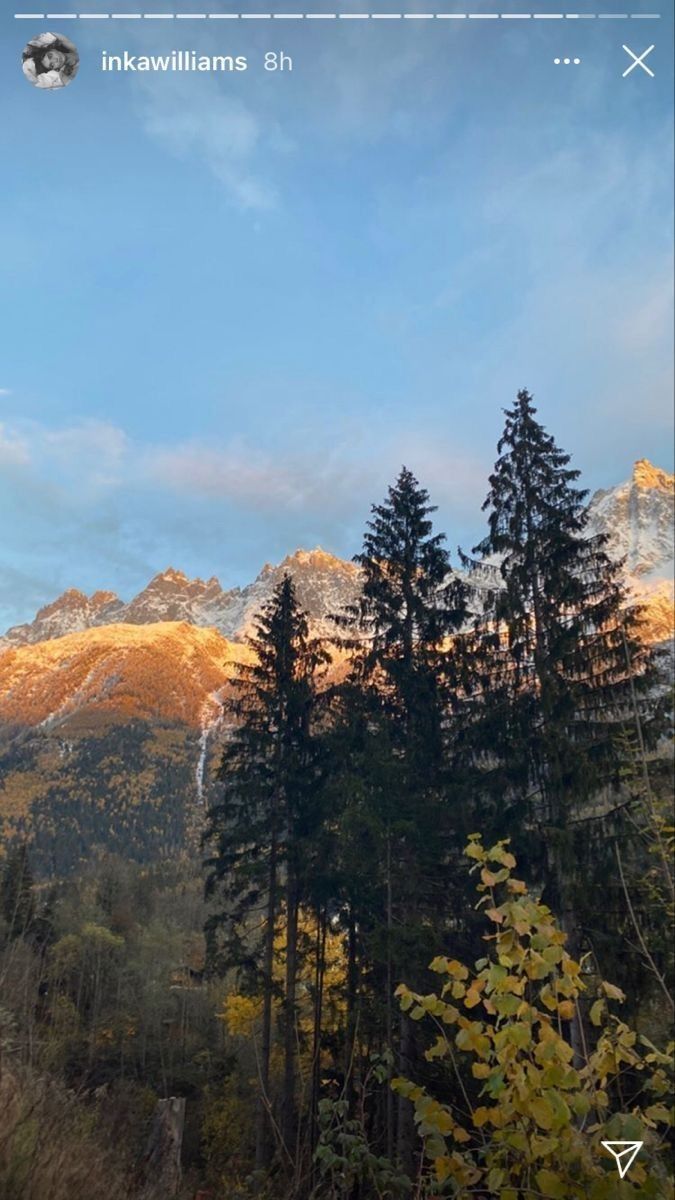 the mountains are covered in snow and trees with yellow leaves on them, against a blue sky