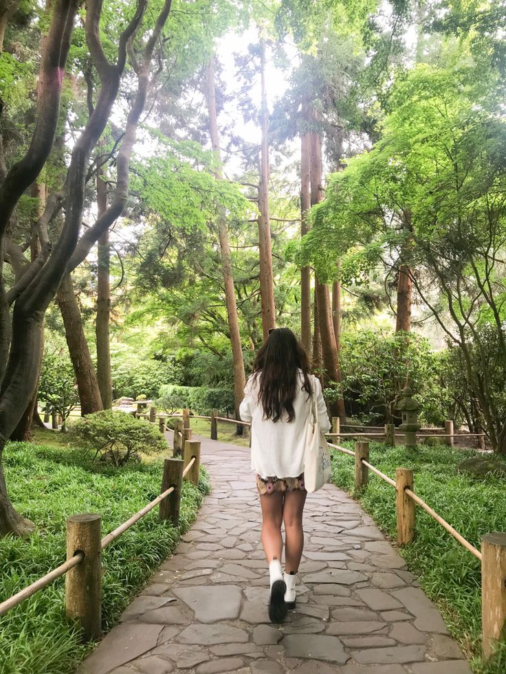 a woman walking down a path through a lush green forest