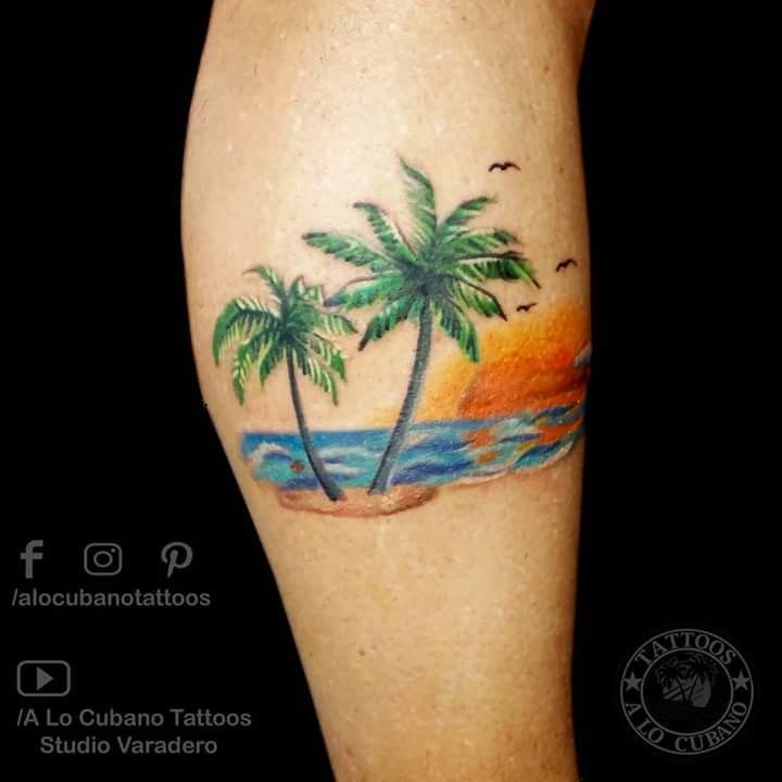 a palm tree tattoo on the left leg with an ocean and sunset in the background