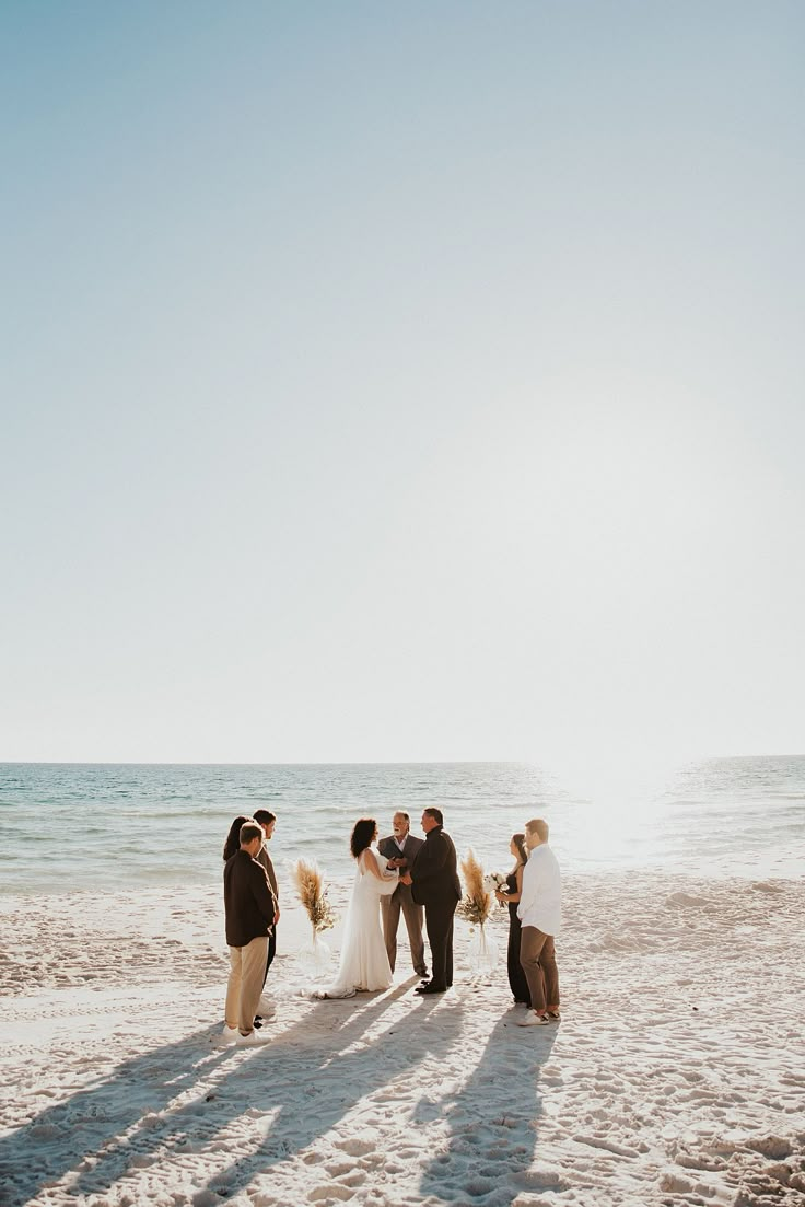 a group of people standing on top of a sandy beach next to the ocean and water