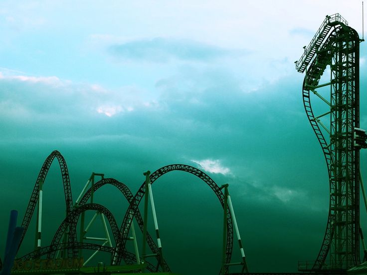 an amusement park roller coaster against a blue sky with dark clouds in the background,