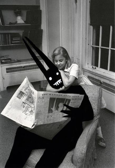 a woman sitting in a chair reading a newspaper with a cat mask on her head