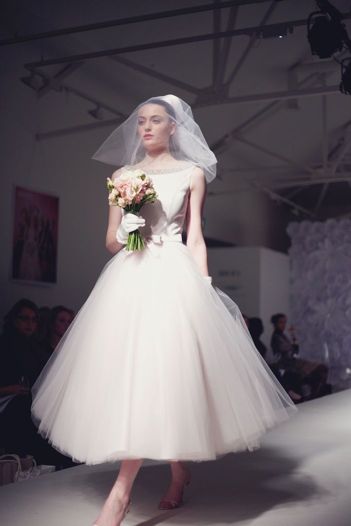 a woman in a white dress and veil walking down the runway at a fashion show