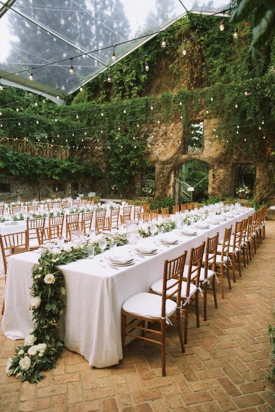 the table is set up with white linens and greenery for an outdoor wedding