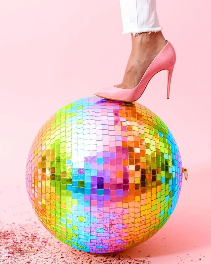 a woman in high heels standing on top of a disco ball with her legs up