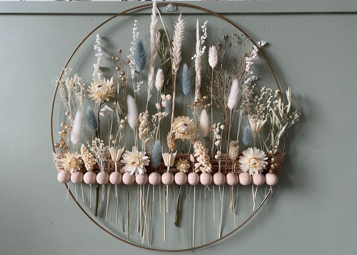 an arrangement of dried flowers and plants on a circular metal rack hanging on the wall