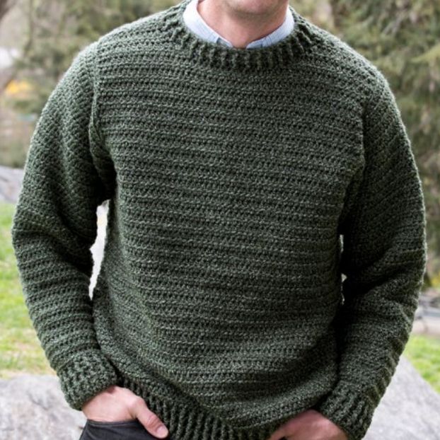 a man standing in front of a rock wearing a green knitted sweater and black pants