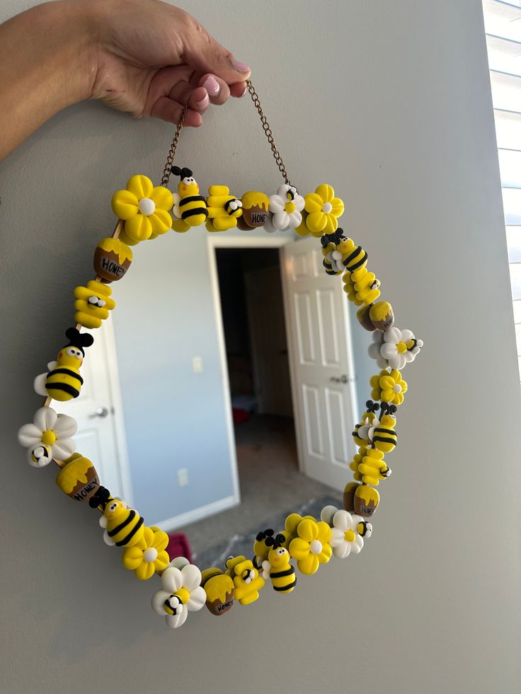 a hand holding a mirror decorated with yellow and black bees on it's chain