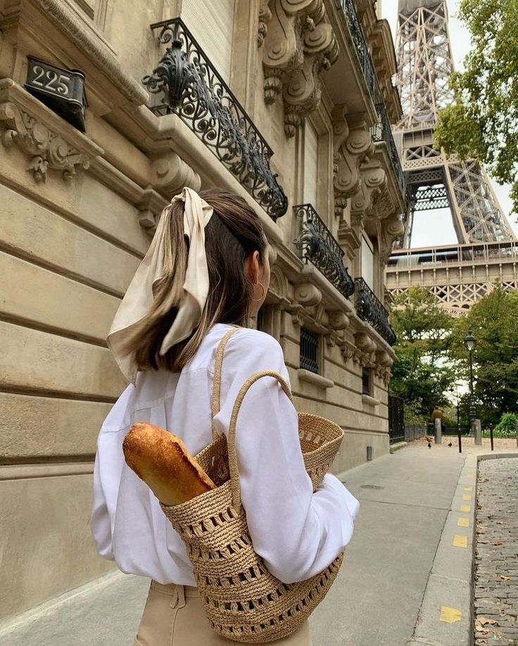 a woman is walking down the street carrying a baguette in front of the eiffel tower