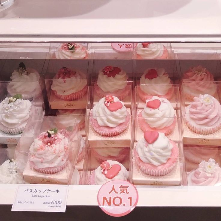 a display case filled with lots of cupcakes in pink and white frosting