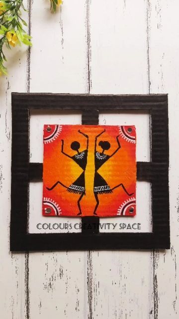 an orange and black wall hanging on a white wooden wall with flowers in the background