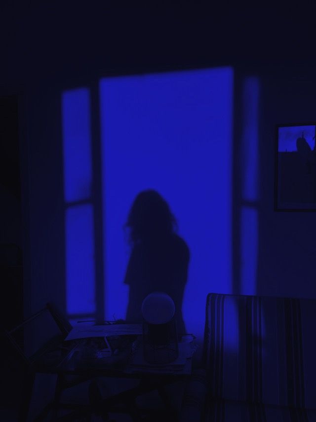 a person standing in front of a window with blue light coming through the windows and their shadow on the table