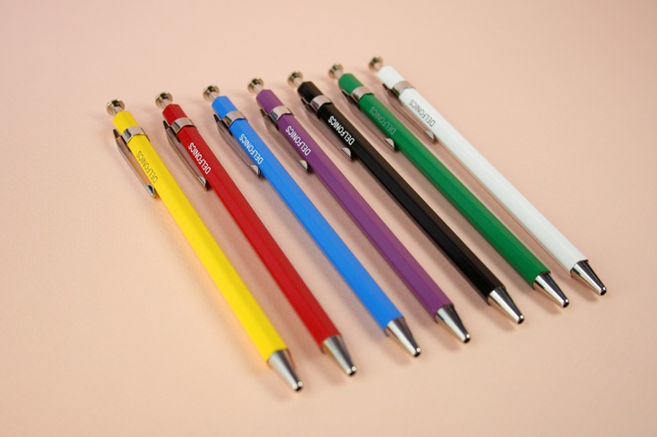 six different colored pens lined up next to each other on a pink surface with one pen in the middle