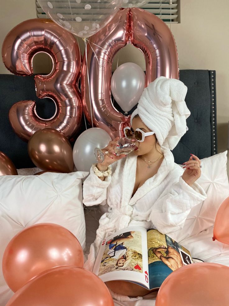 a woman sitting on a bed reading a book with balloons in the air behind her