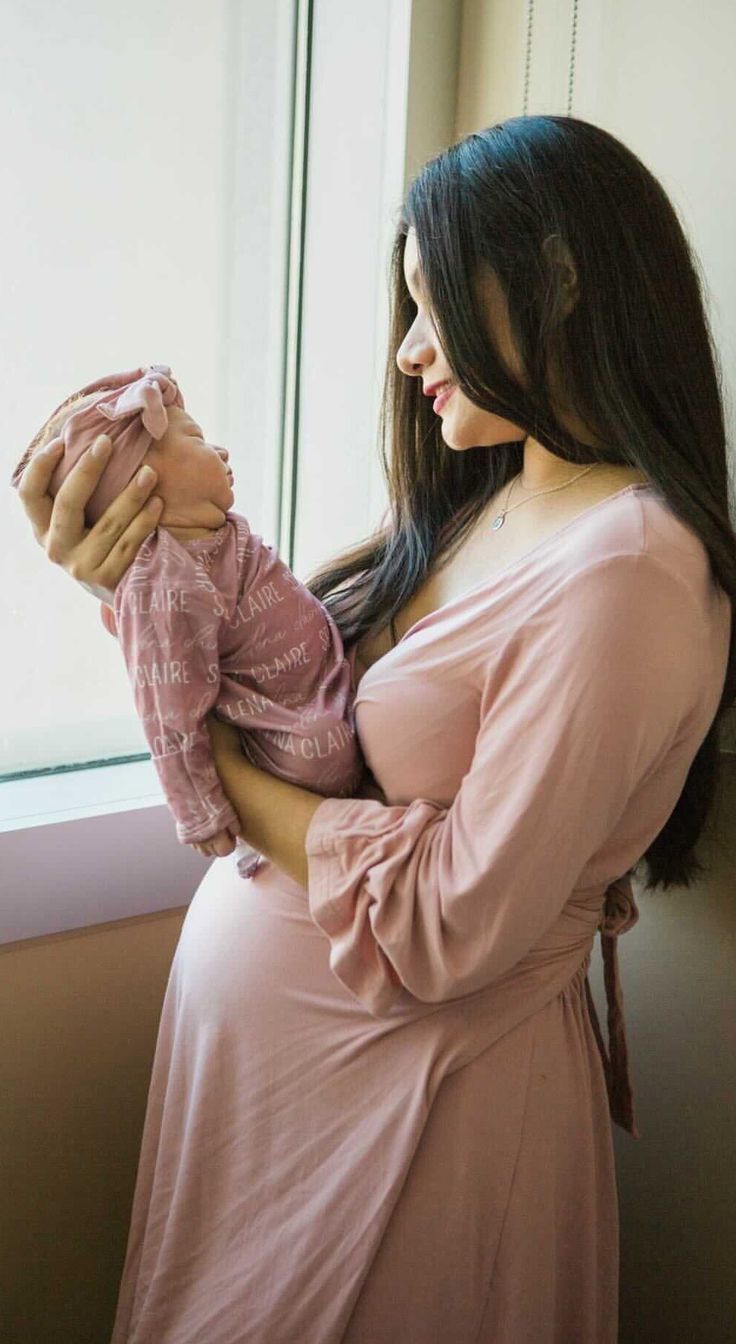 a woman holding a baby in her arms looking out the window at the outside world