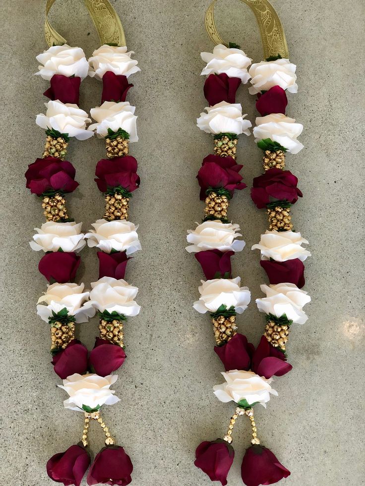 two red and white flowers are attached to some gold hooks on the wall with other decorations hanging from them