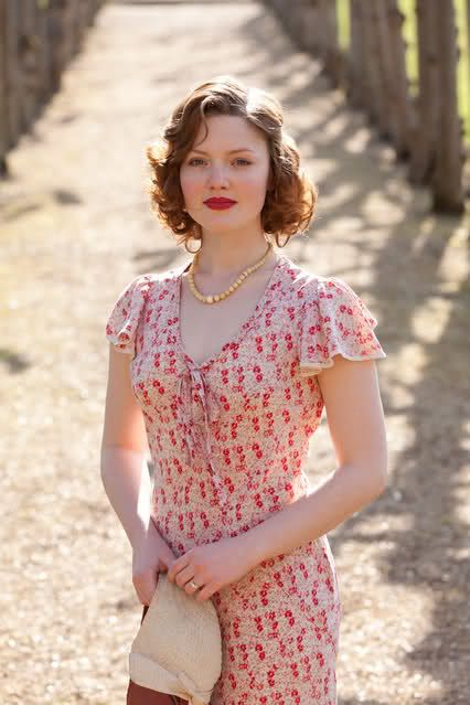 a woman in a dress and hat standing on a dirt road