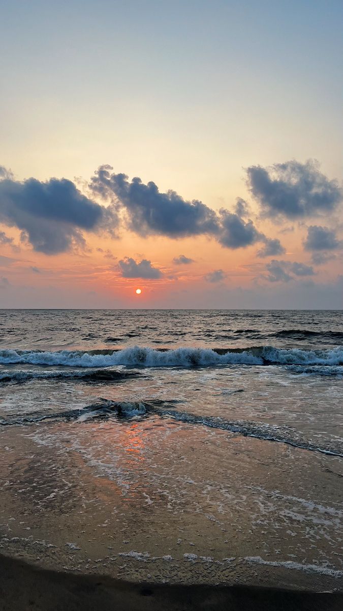 the sun is setting over the ocean with waves crashing in front of it and some clouds