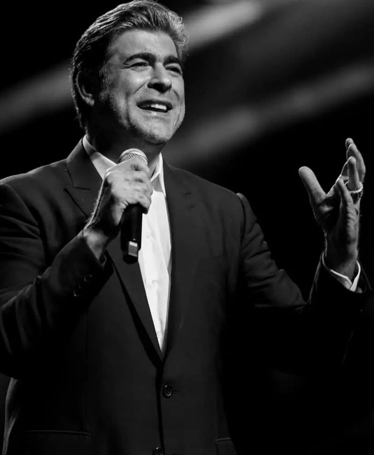 a black and white photo of a man in a tuxedo holding a microphone