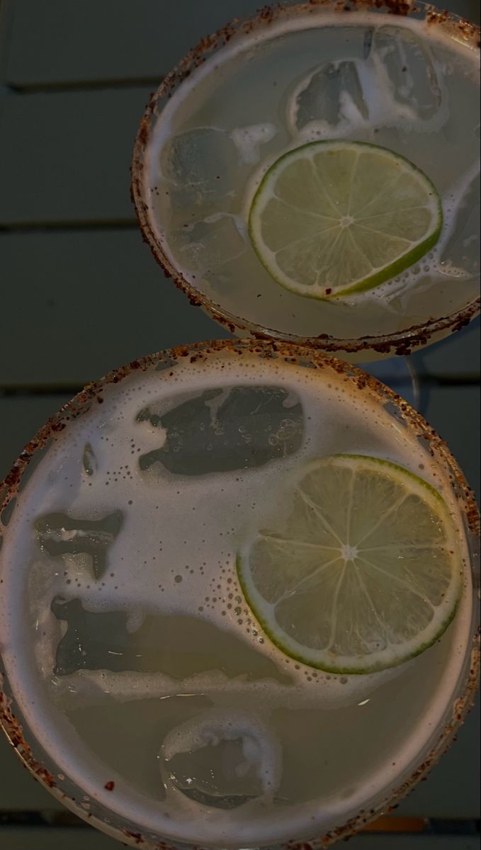 two margaritas with lime slices and ice on the rim, sitting next to each other