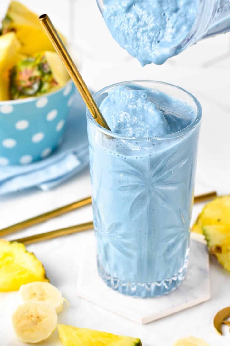 a blue smoothie is being poured into a glass with bananas and other fruit in the background